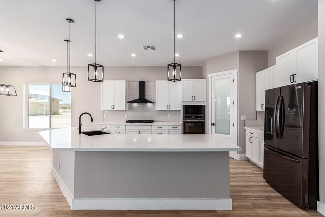 kitchen with pendant lighting, black appliances, sink, wall chimney range hood, and a spacious island