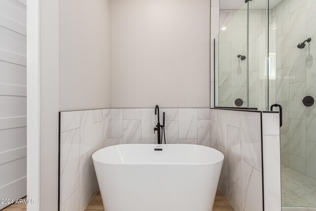 bathroom featuring plus walk in shower and tile walls