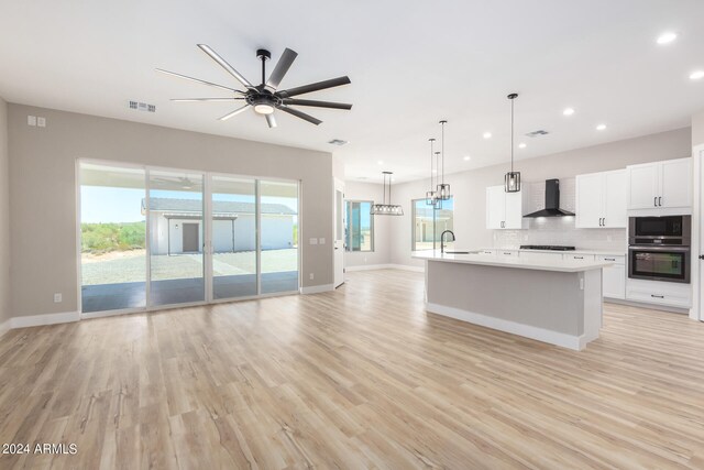 kitchen with appliances with stainless steel finishes, hanging light fixtures, white cabinets, sink, and wall chimney range hood