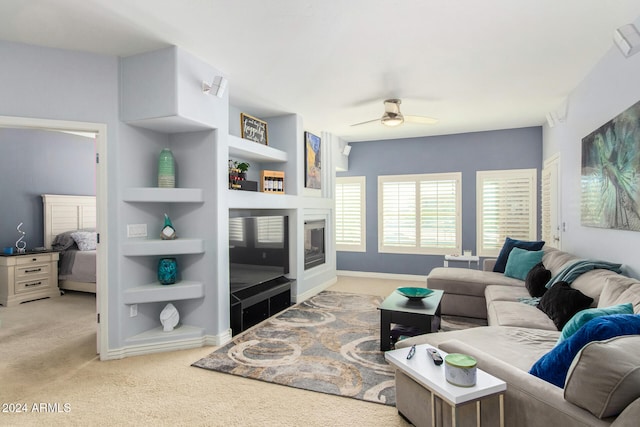 living room with light colored carpet, a fireplace, built in features, and ceiling fan