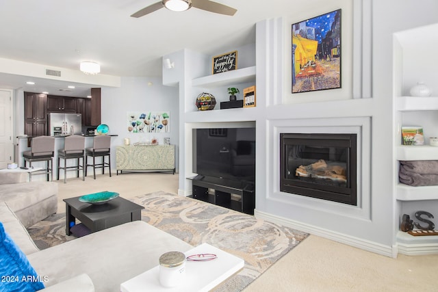 carpeted living room featuring built in shelves and ceiling fan