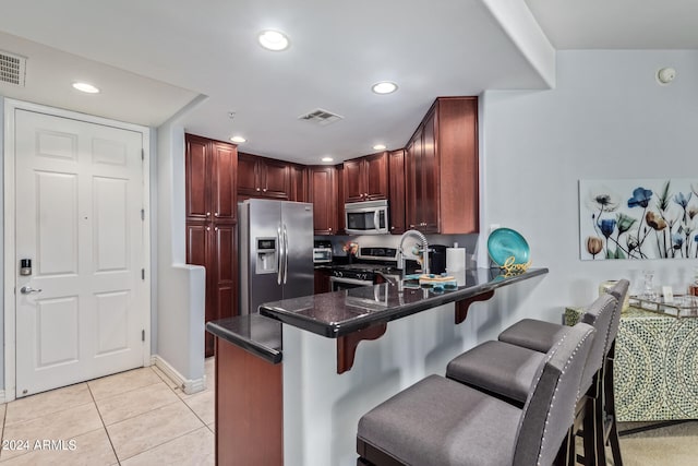 kitchen featuring appliances with stainless steel finishes, a kitchen bar, kitchen peninsula, and light tile patterned floors