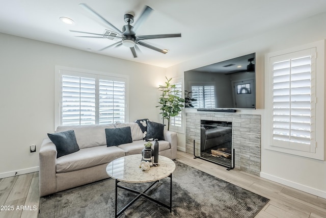 living room with a ceiling fan, baseboards, wood finished floors, and a stone fireplace