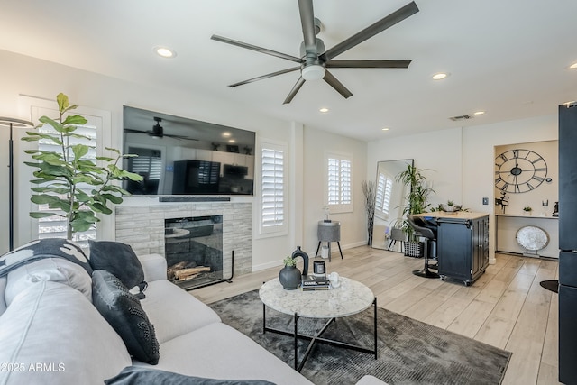 living area featuring light wood finished floors, recessed lighting, visible vents, a glass covered fireplace, and baseboards