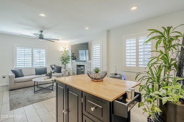 kitchen with a fireplace, recessed lighting, wooden counters, a ceiling fan, and a kitchen island