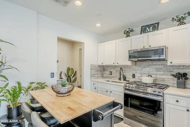 kitchen featuring stainless steel appliances, a sink, white cabinetry, light countertops, and backsplash