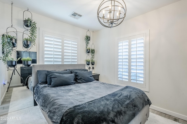 bedroom with a notable chandelier, light wood finished floors, visible vents, and baseboards