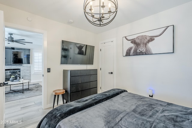 bedroom featuring light wood finished floors, baseboards, an inviting chandelier, and a glass covered fireplace