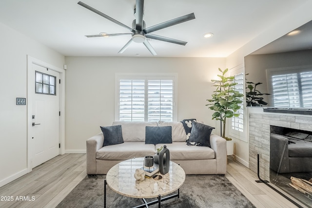 living room featuring a healthy amount of sunlight, wood finished floors, and a stone fireplace