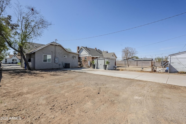 view of front of property with stucco siding, central AC unit, fence, a shed, and an outdoor structure