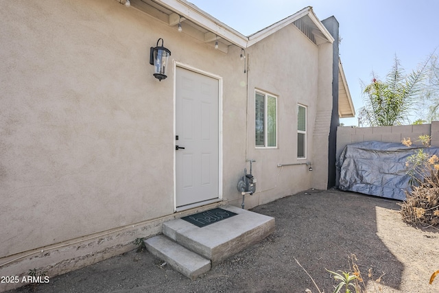 view of exterior entry with fence and stucco siding