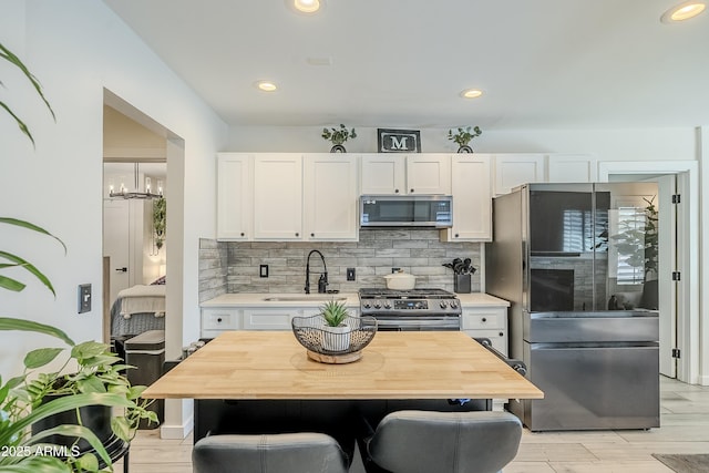 kitchen with a sink, white cabinets, appliances with stainless steel finishes, backsplash, and light wood finished floors