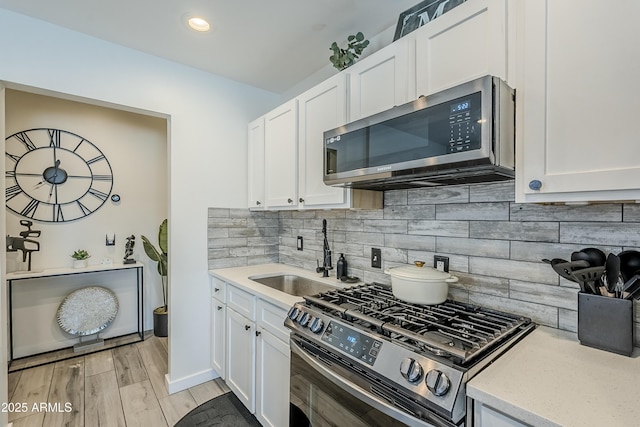 kitchen featuring tasteful backsplash, white cabinets, stainless steel appliances, light wood-style floors, and a sink