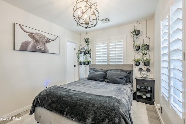 bedroom with a chandelier, wood finished floors, visible vents, and baseboards