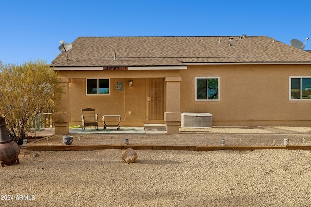 rear view of property featuring roof with shingles, cooling unit, and stucco siding