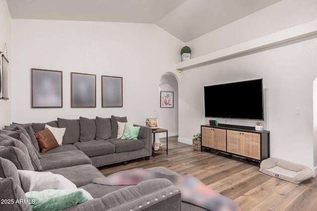 living area featuring lofted ceiling, arched walkways, baseboards, and wood finished floors
