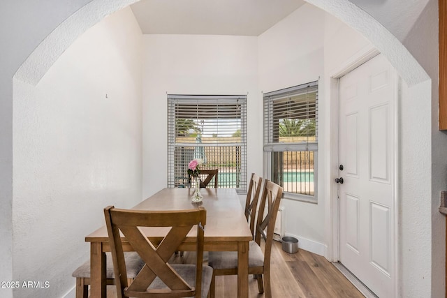 dining room with arched walkways, baseboards, and light wood-type flooring