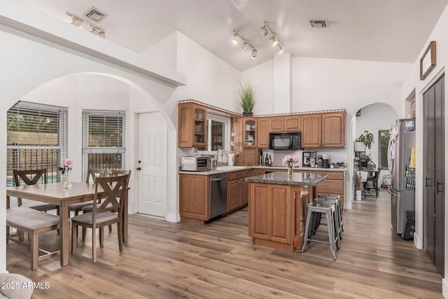 kitchen with a center island, glass insert cabinets, arched walkways, brown cabinets, and appliances with stainless steel finishes