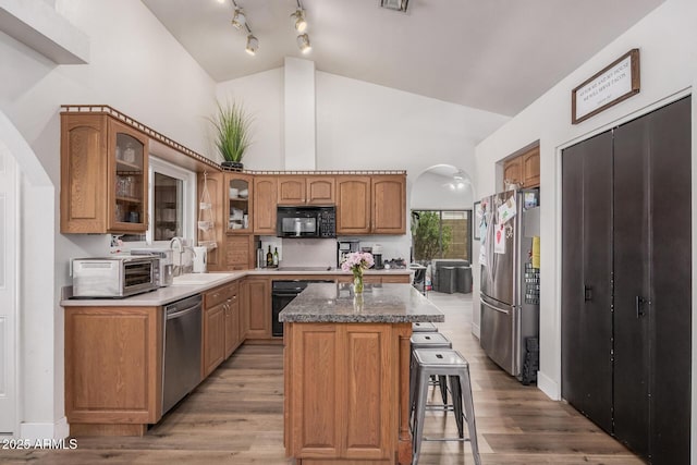 kitchen featuring a toaster, a center island, glass insert cabinets, a sink, and black appliances