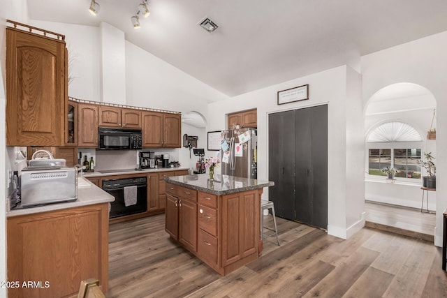 kitchen featuring arched walkways, black appliances, a kitchen breakfast bar, and visible vents