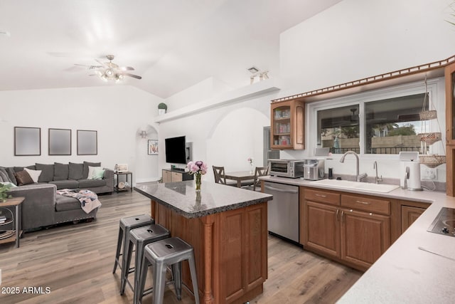 kitchen with a ceiling fan, a sink, a kitchen breakfast bar, arched walkways, and dishwasher