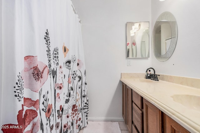 bathroom with double vanity, curtained shower, baseboards, and a sink
