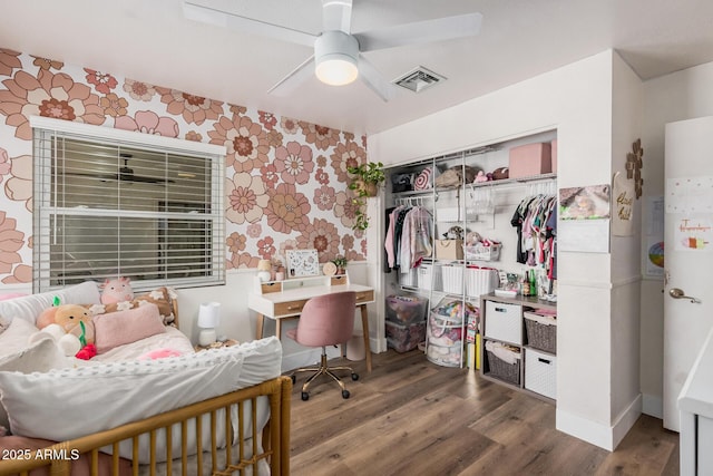 bedroom featuring wood finished floors, wallpapered walls, a closet, visible vents, and an accent wall