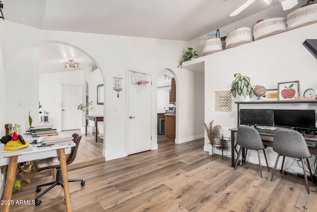 home office with arched walkways, light wood-style floors, ceiling fan, and baseboards