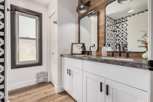 full bathroom featuring double vanity, wood finished floors, baseboards, and a sink