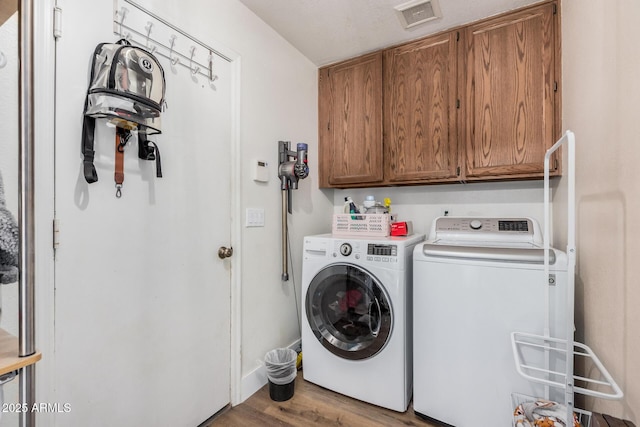 washroom featuring washing machine and clothes dryer, cabinet space, visible vents, and wood finished floors