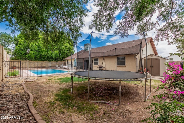 rear view of house with a storage unit, an outdoor structure, a trampoline, and a fenced backyard