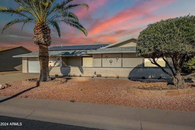 view of front of home with a garage, driveway, roof mounted solar panels, and brick siding