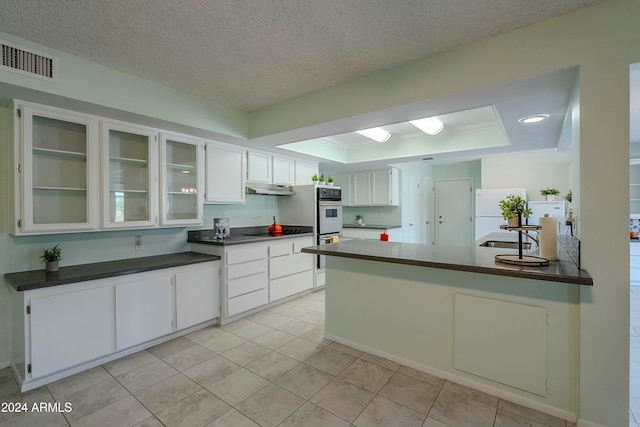 kitchen featuring white cabinets, white appliances, kitchen peninsula, and a raised ceiling