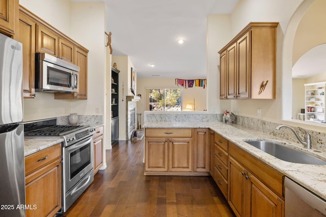 kitchen featuring stainless steel appliances, sink, light stone counters, kitchen peninsula, and dark hardwood / wood-style floors