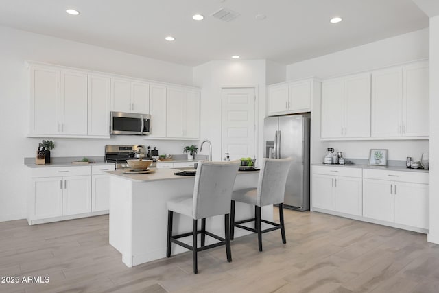 kitchen with a breakfast bar area, white cabinetry, stainless steel appliances, light hardwood / wood-style floors, and an island with sink