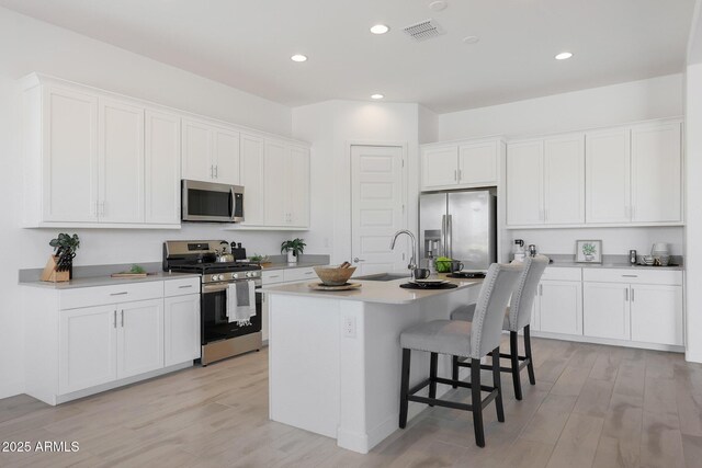 kitchen with a kitchen island with sink, sink, white cabinets, and appliances with stainless steel finishes