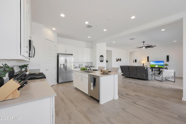 kitchen with sink, light wood-type flooring, appliances with stainless steel finishes, an island with sink, and white cabinets