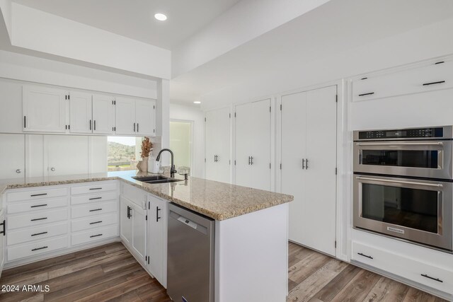 kitchen with kitchen peninsula, stainless steel appliances, sink, hardwood / wood-style flooring, and white cabinets