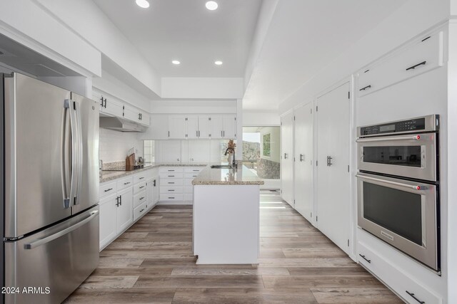 kitchen with appliances with stainless steel finishes, light stone counters, sink, white cabinets, and an island with sink