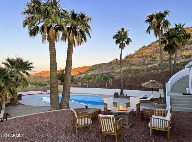 pool at dusk with a patio area, a mountain view, and an outdoor fire pit