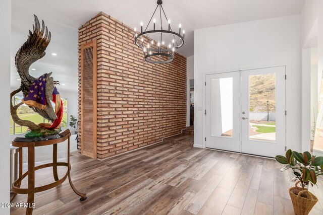 entryway with french doors, a high ceiling, brick wall, a chandelier, and wood-type flooring