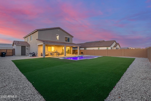 back of property at dusk featuring a patio, a tiled roof, a fenced backyard, and a lawn