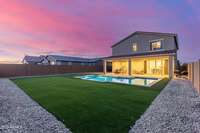 back of property at dusk featuring a fenced in pool, a lawn, stucco siding, a fenced backyard, and a patio area