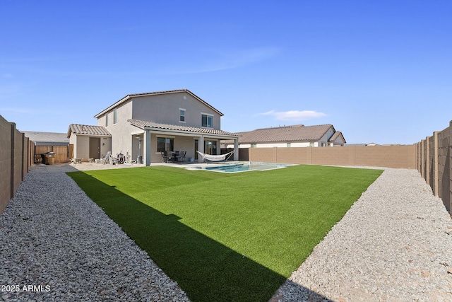 back of property with a lawn, a tile roof, a fenced backyard, a fenced in pool, and a patio area