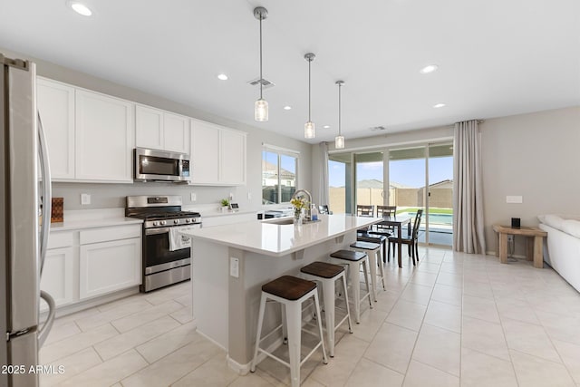 kitchen featuring a center island with sink, a sink, white cabinetry, stainless steel appliances, and light countertops