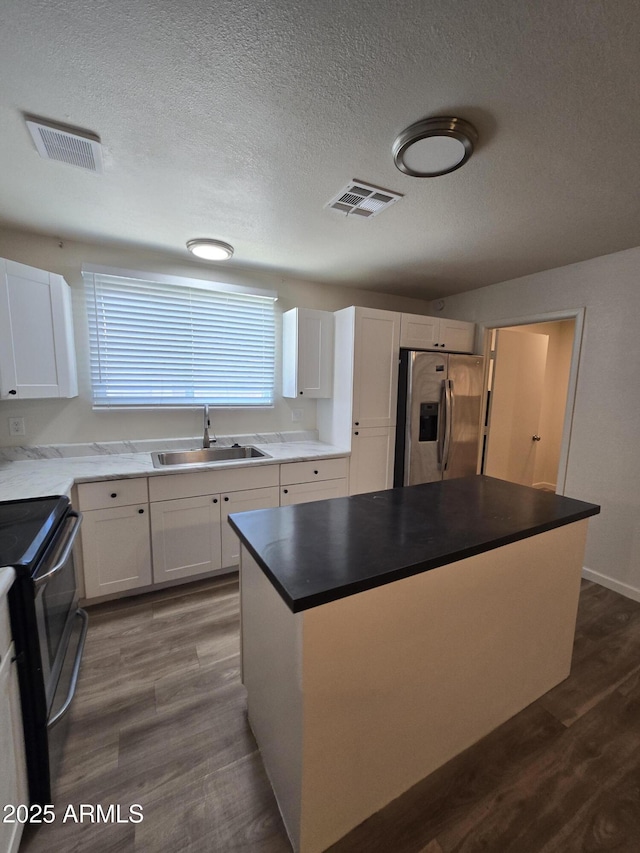 4911 W Merrell St, Phoenix, AZ 85031 - kitchen featuring stainless steel appliances, white cabinets, a textured ceiling, a center island, and dark wood-type flooring