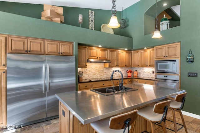 kitchen featuring a high ceiling, sink, built in appliances, and an island with sink