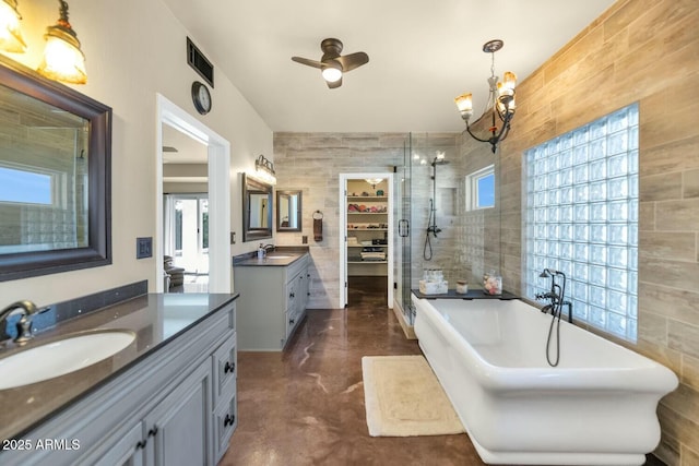 bathroom with separate shower and tub, vanity, tile walls, concrete flooring, and ceiling fan with notable chandelier