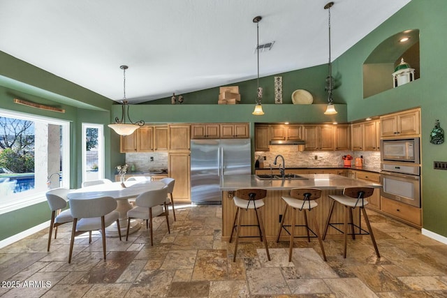 kitchen with an island with sink, tasteful backsplash, high vaulted ceiling, built in appliances, and sink