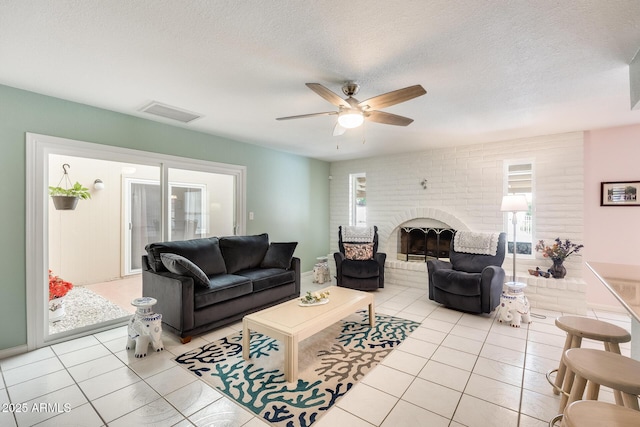 living area featuring a ceiling fan, a brick fireplace, a textured ceiling, visible vents, and light tile patterned flooring